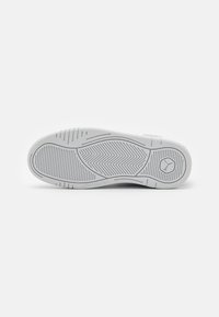 Suola di scarpa atletica bianca con una superficie in gomma testurizzata, caratterizzata da un motivo a spina di pesce e scanalature verticali per una migliore aderenza. Dettaglio del logo sul lato.
