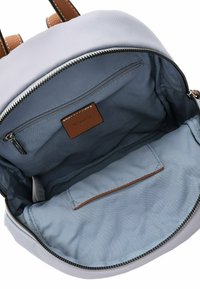 Un sac à dos gris clair avec des accents en cuir brun, comportant un compartiment principal zippé et une poche intérieure. Texture lisse, design structuré.