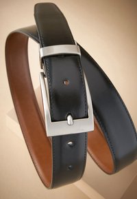 Czarny skórzany pasek z metalową, srebrną klamrą, o gładkiej fakturze i widocznym przeszyciu, z kilkoma otworami do regulacji oraz brązowym wnętrzem.