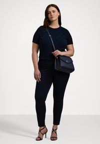 Marinblå stickad topp med kort ärm och mönster, i kombination med åtsittande marinblå byxor och sandaletter med remmar. Inkluderar en mörk axelväska.