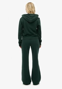 Sudadera verde oscuro con pantalones acampanados a juego. Material de mezcla de algodón, puños acanalados y capucha. Diseño simple sin patrones ni acentos visibles.