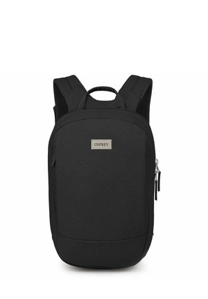 Mochila negra con un acabado de tela suave, que cuenta con correas ajustables, un mango superior y una forma rectangular. Incluye un bolsillo exterior con cremallera.