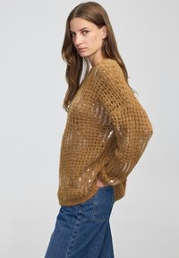 Brązowy sweter dzianinowy o luźnym, teksturowanym wzorze; ma szersze rękawy, wygodne dopasowanie oraz subtelny blask od cekinów.