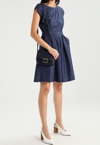 Námořnické modré džínové šaty s krátkými rukávy, skládací sukní a kapsami. V kombinaci s malou černou kabelkou přes rameno a bílými lodičkami.