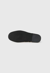 Svart gummisåle med teksturert overflate, avrundet form og minimalistisk design. Har små sirkulære detaljer langs kanten.