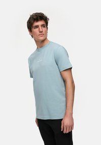 Lys blå bomull t-skjorte med rund hals og korte ermer; har en liten, hvit logo på brystet og en vanlig passform.