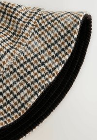 Wool hat with a houndstooth pattern in tan, black, and white. Features a soft, textured surface and a black ribbed brim.