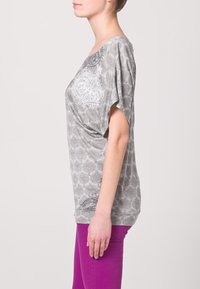 Top gris de manga corta con cuello redondo, que presenta un patrón intrincado. Combinado con pantalones ajustados de un vibrante color púrpura.