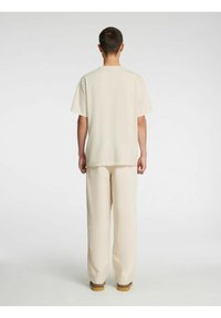 Heledast beežist puuvillane lühikeste varrukatega T-särk, mida on sobitatud samas toonis laia lõikega pükstega, omades lõdvestunud istuvust ja minimaalset õmblust, et tagada ühtlane tekstuur.