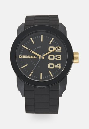 Montre-bracelet Diesel noire avec index et chiffres dorés 02, 03, 04, aiguilles dorées, bracelet en caoutchouc et couronne dorée sur le côté droit.
