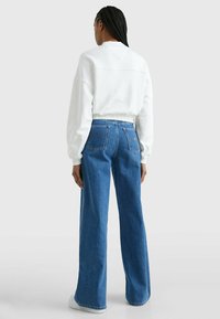 Sudadera blanca con escote redondeado y hombros caídos, combinada con vaqueros azul ancho de pierna con bolsillos traseros y lavado claro.