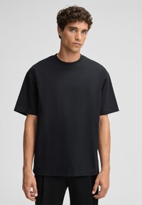 Schwarzes kurzärmliges T-Shirt aus weicher Baumwolle mit Rundhalsausschnitt, das einen lockeren Schnitt und eine glatte Textur bietet.