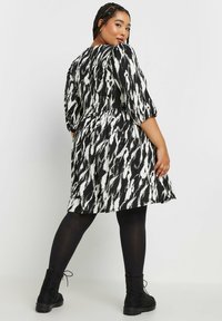 Svart och vit klänning med abstrakt mönster, puffärmar, åtdragen midja och utställd fåll, i kombination med svarta ankelstövlar och strumpbyxor.