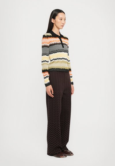 Maglione lavorato a maglia con motivo a zigzag in multicolori (arancione, giallo, verde, nero) e colletto nero compatto. Pantaloni marroni con motivo a zigzag.