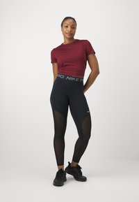 Bordeaux lyhythihainen urheiluvaate, jossa on logo, yhdistettynä mustiin legginsseihin, joissa on verkkopaneeleja, erottuva vyötäröosa ja mustat lenkkarit.
