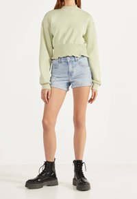 Sudadera corta verde claro con bajo fruncido, combinada con shorts de mezclilla azul claro desgastados. Completado con botas de combate negras con cordones.