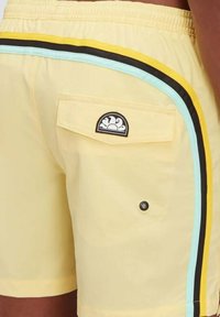 Costumi da bagno gialli con tasca posteriore a pattina, toppa con logo nera e righe orizzontali in nero, giallo e azzurro chiaro.