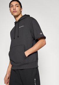 Μαύρο φούτερ με κουκούλα και κοντά μανίκια, με μπροστινή τσέπη και κεντημένο λογότυπο. Κατασκευασμένο από μαλακό, υφασμάτινο ύφασμα με υφή.