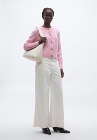 Rózsaszín kötött kardigán arany gombokkal, széles fehér nadrággal és krémszínű válltáskával párosítva. A megjelenést fekete sarokkal ellátott csizmák egészítik ki.