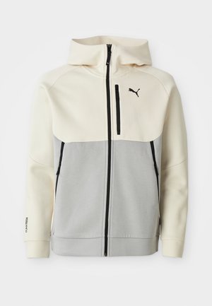 Puma capuchonjack met een crèmekleurig bovenstuk en een grijs onderstuk, voorzien van een rits aan de voorkant, twee zakken en zwarte logo-accenten.