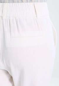 Pantalons en lin blanc avec une taille smockée et une poche arrière ornée d'une couture. Texture douce et tissu léger.