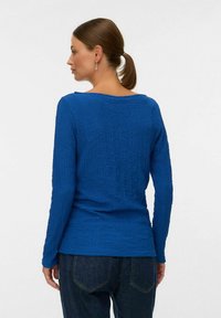 Maglia azzurra a maniche lunghe con texture e scollatura rotonda, caratterizzata da una vestibilità ampia e cuciture orizzontali. Indossata con jeans scuri.