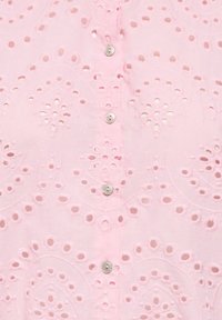 Tissu rose avec des motifs floraux découpés brodés et une rangée verticale de petits boutons blancs.