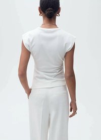 Top alb potrivit, cu mâneci scurte și o textură specială, asociat cu pantaloni albi cu talie înaltă, care au două buzunare la spate.