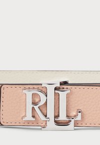 Ceinture en cuir avec une bande texturée rose, un doublure intérieure blanche et une boucle en métal argenté avec le logo RL. Les coutures sur le bord sont visibles.