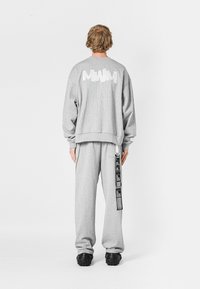 Sudadera gris con gráfico blanco en la parte posterior, combinada con pantalones de chándal grises a juego que presentan un acento de etiqueta negra. Fabricación de suave mezcla de algodón.