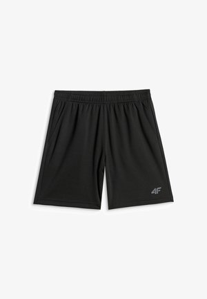 Enfant debout portant un t-shirt blanc uni, un short noir, des chaussettes blanches avec des rayures noires, et des baskets noires et blanches sur un fond gris.