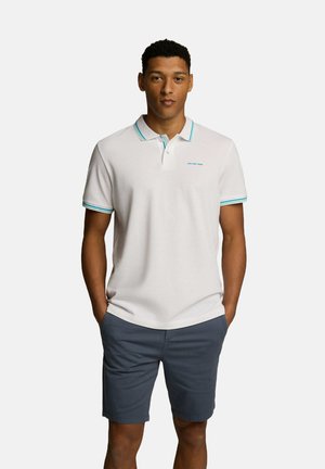 Biała koszulka polo z turkusowymi akcentami na kołnierzyku i rękawach, noszona z ciemnoszarymi szortami, wyeksponowana na jednolitym tle.