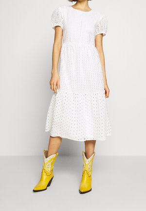 Witte katoenen jurk met pofmouwen en geperforeerd patroon, gelaagde rok. Gecombineerd met gele cowboylaarzen met witte accenten.