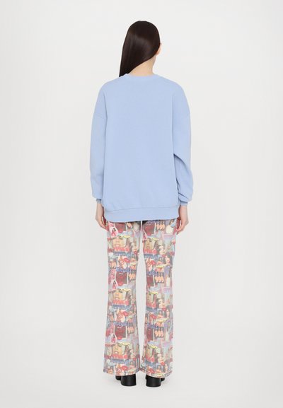 Light blue oversized sweatshirt with a round neckline, paired with colorful flared pants featuring a collage pattern and a smooth texture.