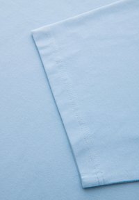 Tissu en coton bleu clair avec un ourlet à double surpiqûre soigneusement cousu le long du bord.