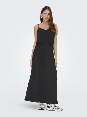 Robe maxi noire avec des bretelles fines, taille élastique, tissu fluide et texture lisse, assortie à des chaussures de sport blanches et noires.
