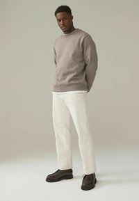 Sudadera gris con cuello redondo, camisa blanca debajo, combinada con jeans de color claro y zapatos de cordones oscuros. Diseño minimalista y corte casual.