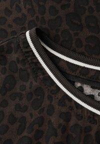 Indumento con stampa leopardata su sfondo marrone scuro. Presenta macchie nere, una scollatura rotonda e dettagli a strisce bianche e nere a contrasto.