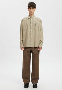 Beige stripete langermet skjorte med brystlomme og grafisk broderi, kombinert med brune vide bukser og svarte sko.