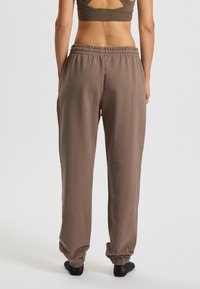 Hnedé joggery z bavlneného zmesi s elastickým pásom, voľným strihom a zúženými manžetami. Hladká textúra a minimalistický dizajn.