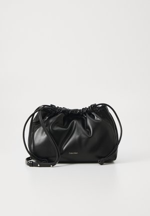 Bolso de hombro Calvin Klein de cuero negro con parte superior fruncida y correa ajustable sobre un fondo blanco liso.