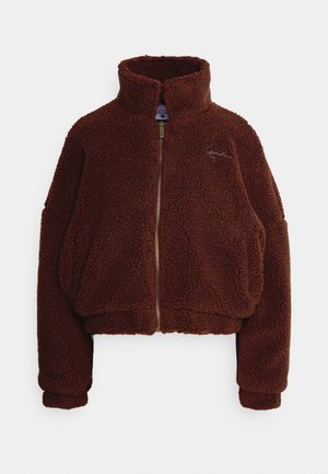 Brown fleece jacket with a high collar, full front zipper, and slightly cropped design. Features oversized sleeves and embroidered logo detail.