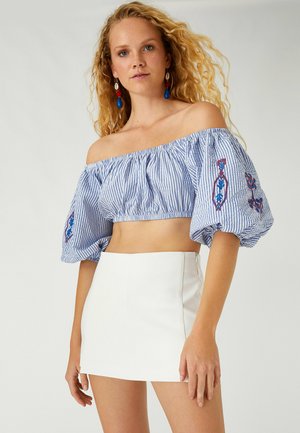 Blå- og hvidstribet off-the-shoulder crop top med puffærmer; har broderede detaljer. Sættes sammen med en tætsiddende hvid mini nederdel.