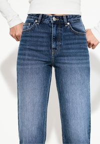 Tmavě modré džíny s vysokým pasem a rovnými nohavicemi, s klasickým pětikapesním designem a kontrastním šitím.