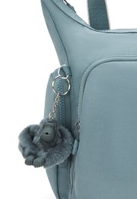 Borsa di tessuto azzurro chiaro con una superficie liscia; presenta una chiusura con zip e un portachiavi a forma di gorilla in peluche attaccato alla zip.