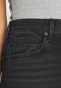 Jeans de mezclilla negra con un diseño clásico, un bolsillo delantero, cierre de botón metálico y una ligera textura.