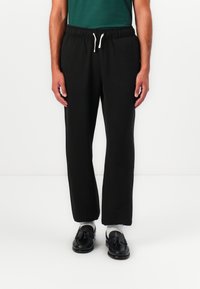 Schwarze Jogginghose mit elastischem Bund und Kordelzug. Glatter Stoff, lockere Passform, gerade Beine, keine sichtbaren Muster oder Akzente.