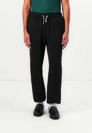 Pantalon de survêtement noir avec une taille élastique et un cordon de serrage. Tissu lisse, coupe ample, jambe droite, sans motifs ni accents visibles.