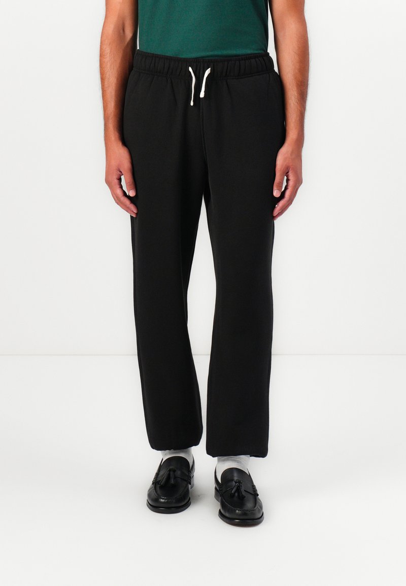 Schwarze Jogginghose mit elastischem Bund und Kordelzug. Glatter Stoff, lockere Passform, gerade Beine, keine sichtbaren Muster oder Akzente.