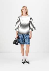 Stripet svart og hvit oversized topp, denimshorts med blå kamuflasjemønster, svart veske, hvite sokker, spisse svarte hæler.